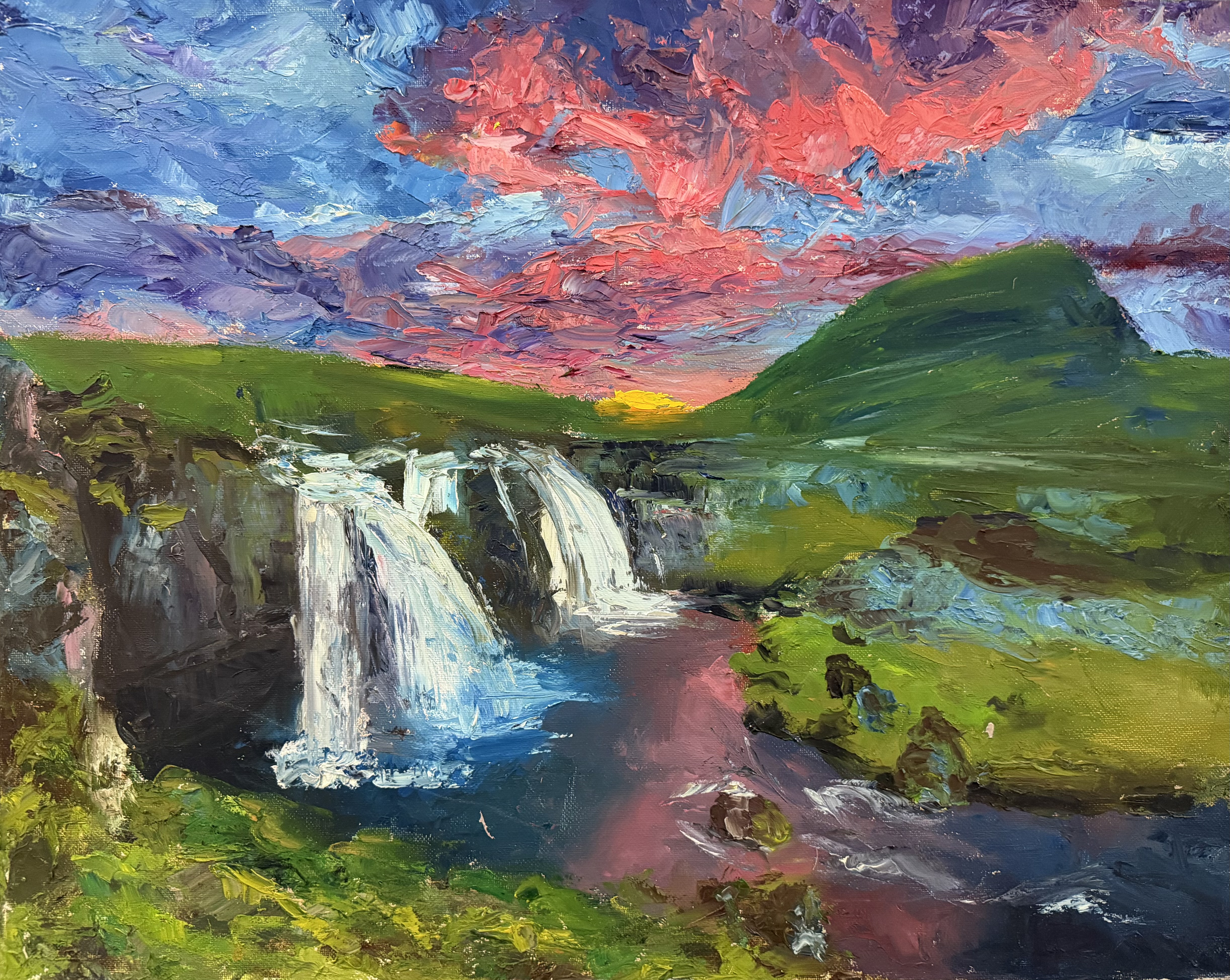 Landscape of a waterfall under a pink and blue sky, with green hills.