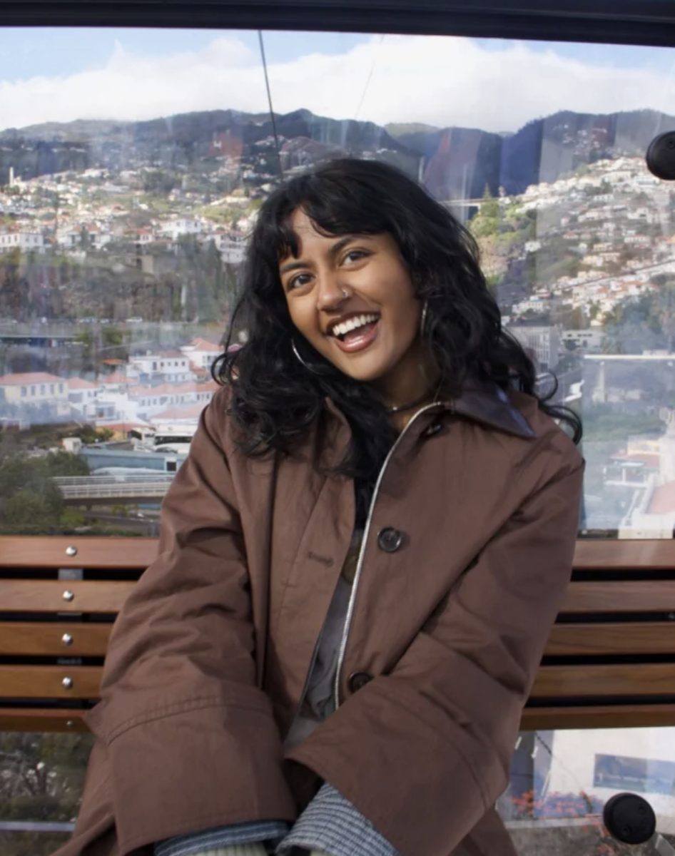 Sahitha Vuddagiri smiling, seated on a bench in a cable car, with a hillside city behind her.