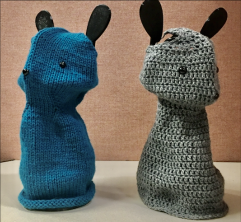 Two crocheted rabbits, one teal and one gray, sitting side by side.
