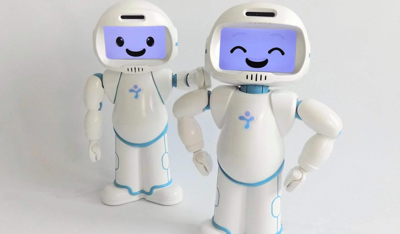 Two small white social robots with smiling faces on their screens.